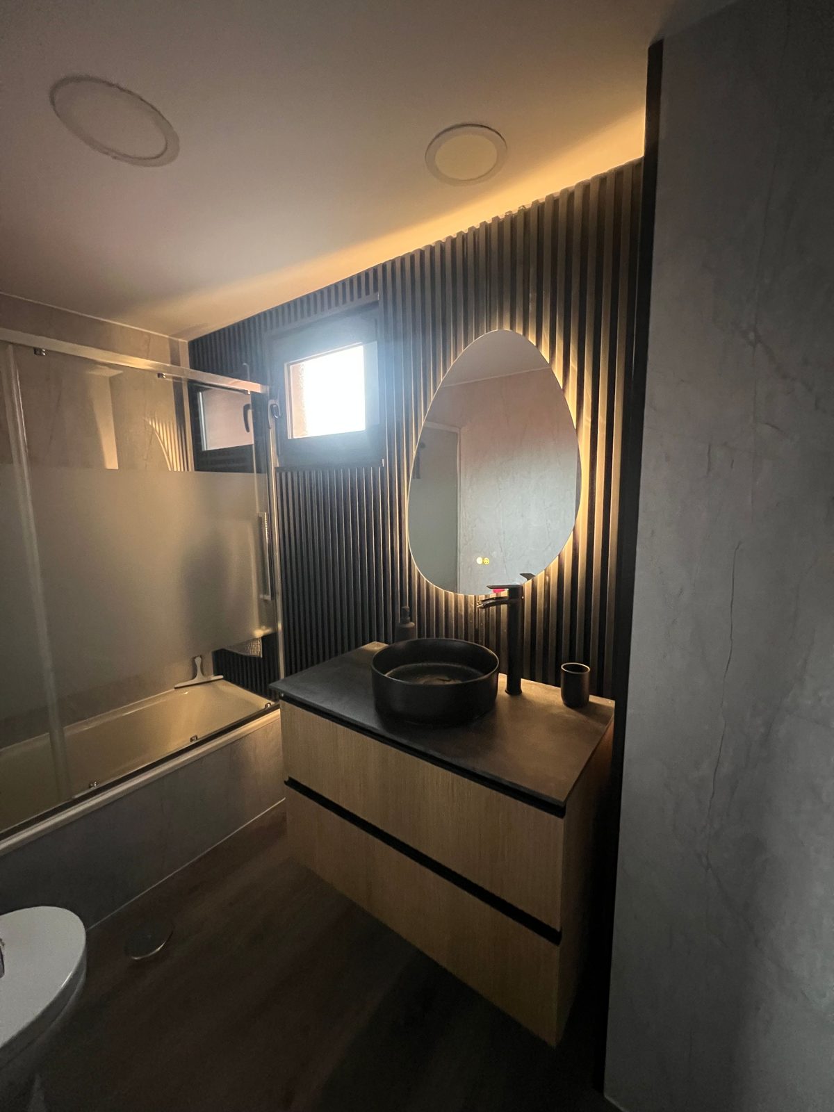 Baño reformado con lamas negras y espejo retroiluminado